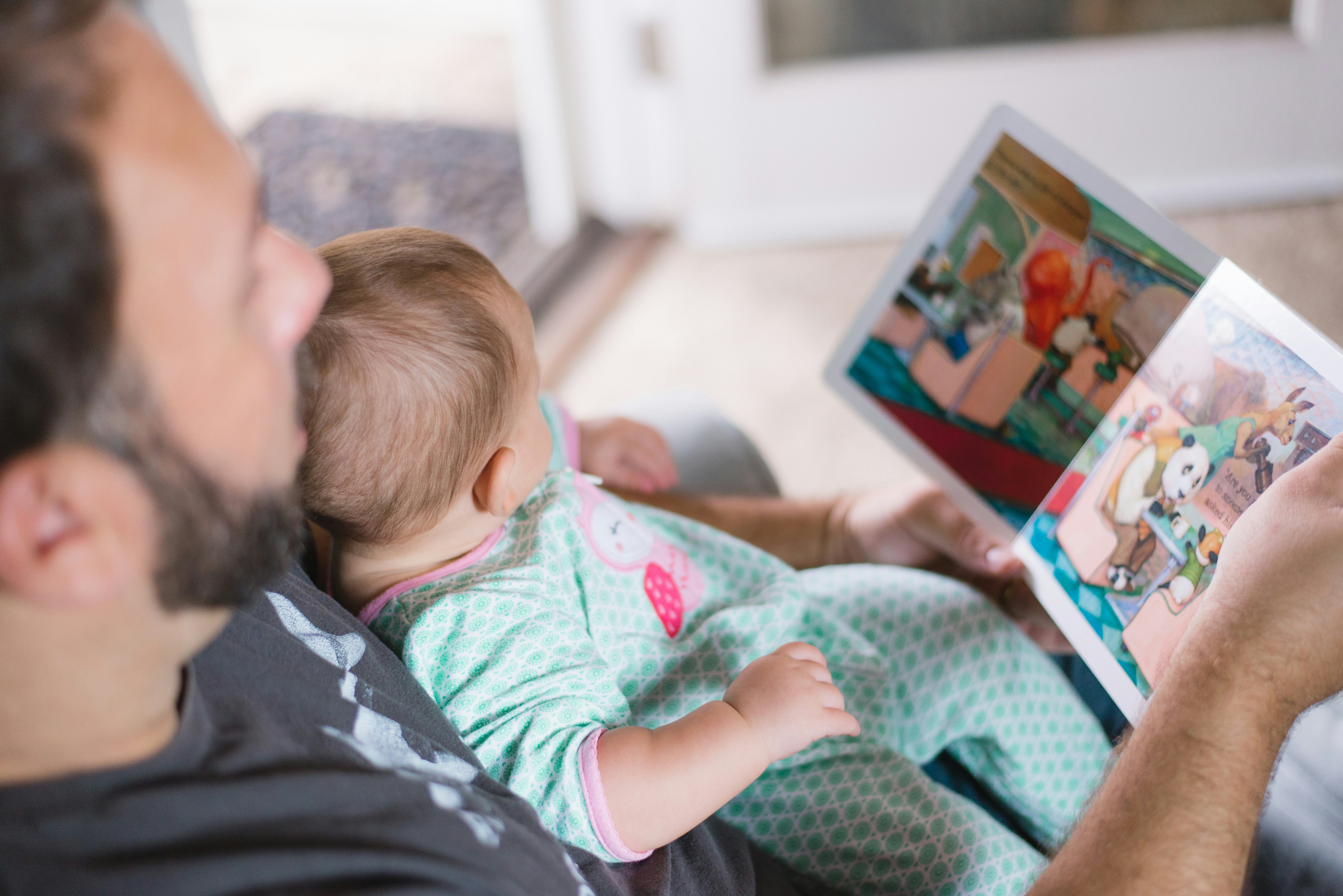 A man reading a children book to his child in his hands